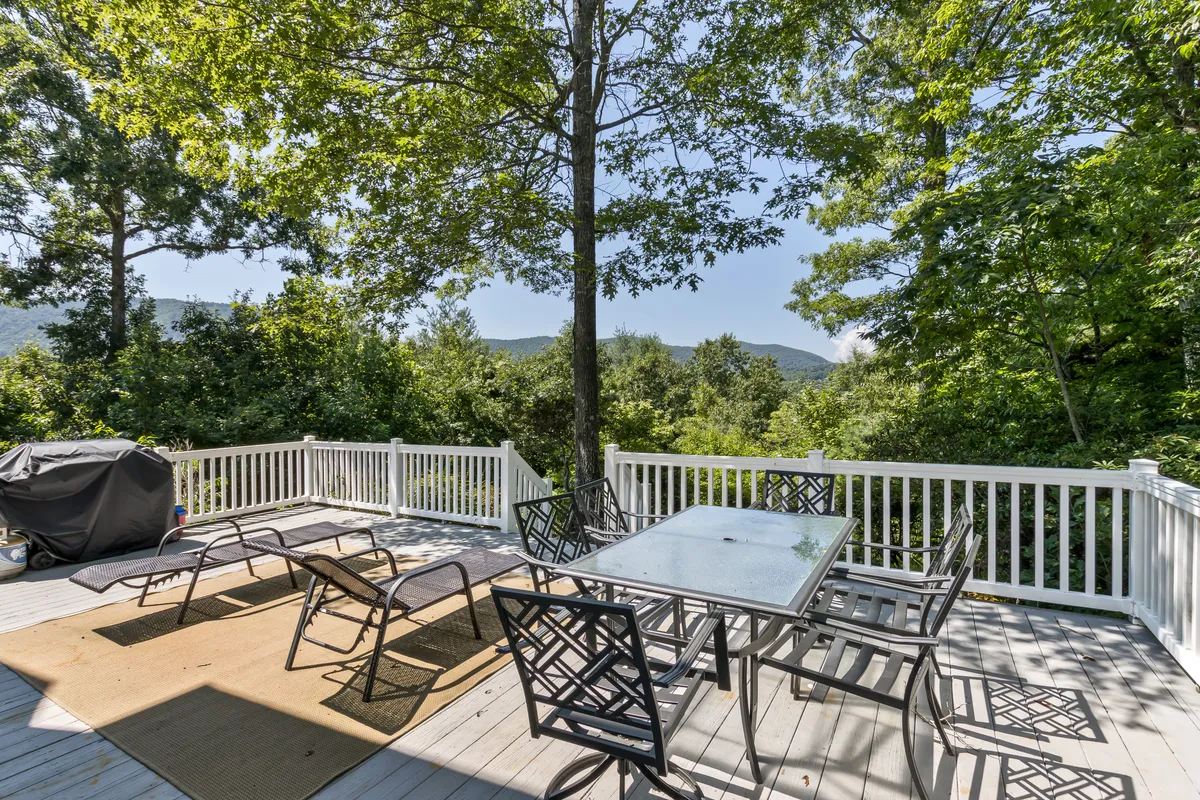 A spacious back deck set against a backdrop of lush greenery and distant mountain views, featuring an outdoor dining set and grill. This inviting space encourages al fresco dining, morning coffee, and sunset conversations surrounded by nature.