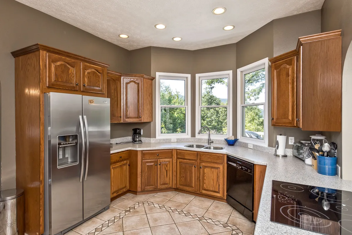 A warm, welcoming kitchen scene featuring spacious countertops, a gleaming stainless steel refrigerator, and ample natural light through multiple windows. The setup suggests a space designed for both serious cooking and relaxed family brunches, with enough room for more than one cook or for gathering around the kitchen.