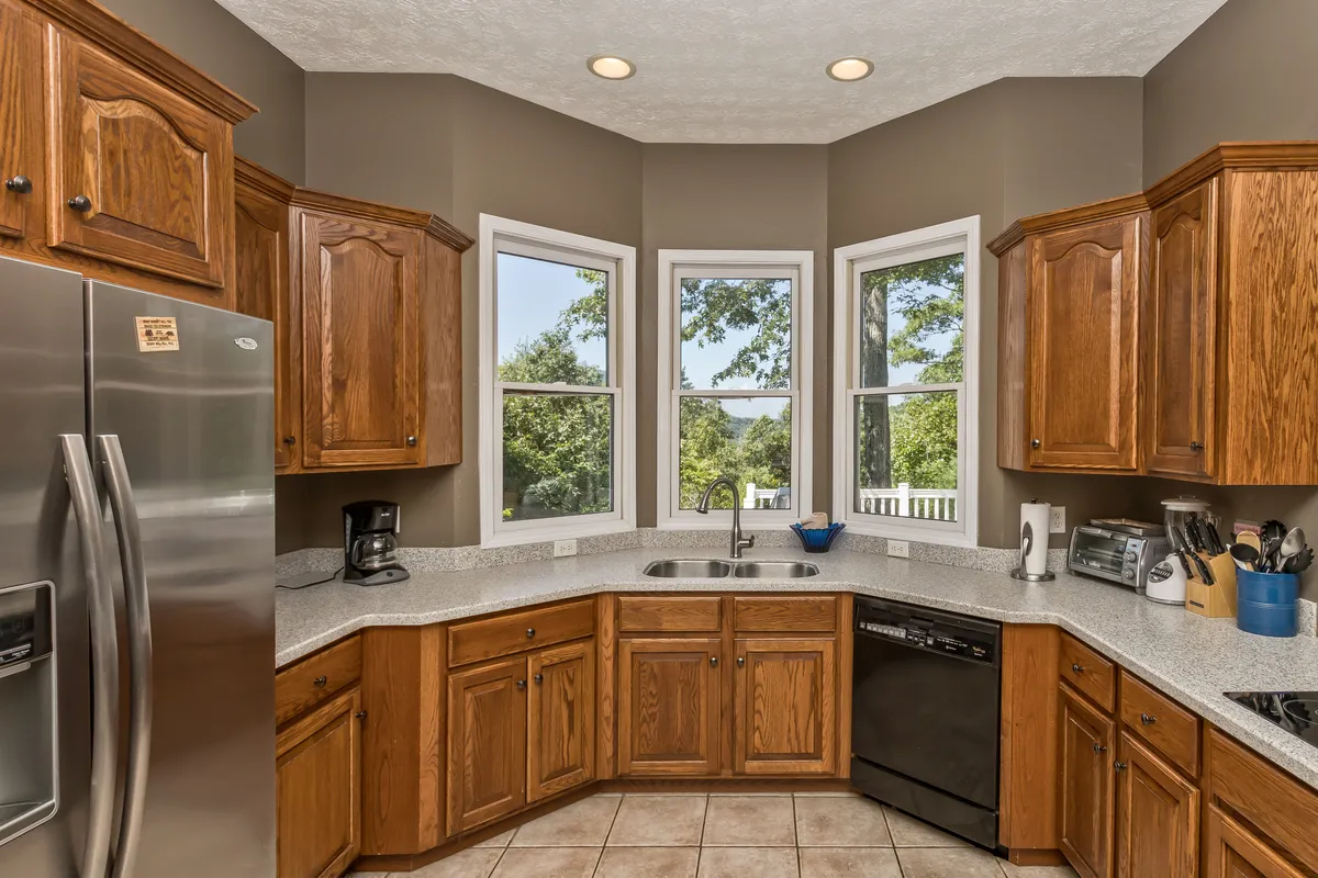 A cozy kitchen corner with sun streaming through wide windows, highlighting a countertop and wooden cabinets. The inviting nook is perfect for enjoying a morning coffee, with views of the outdoors and a sense of warmth and comfort.