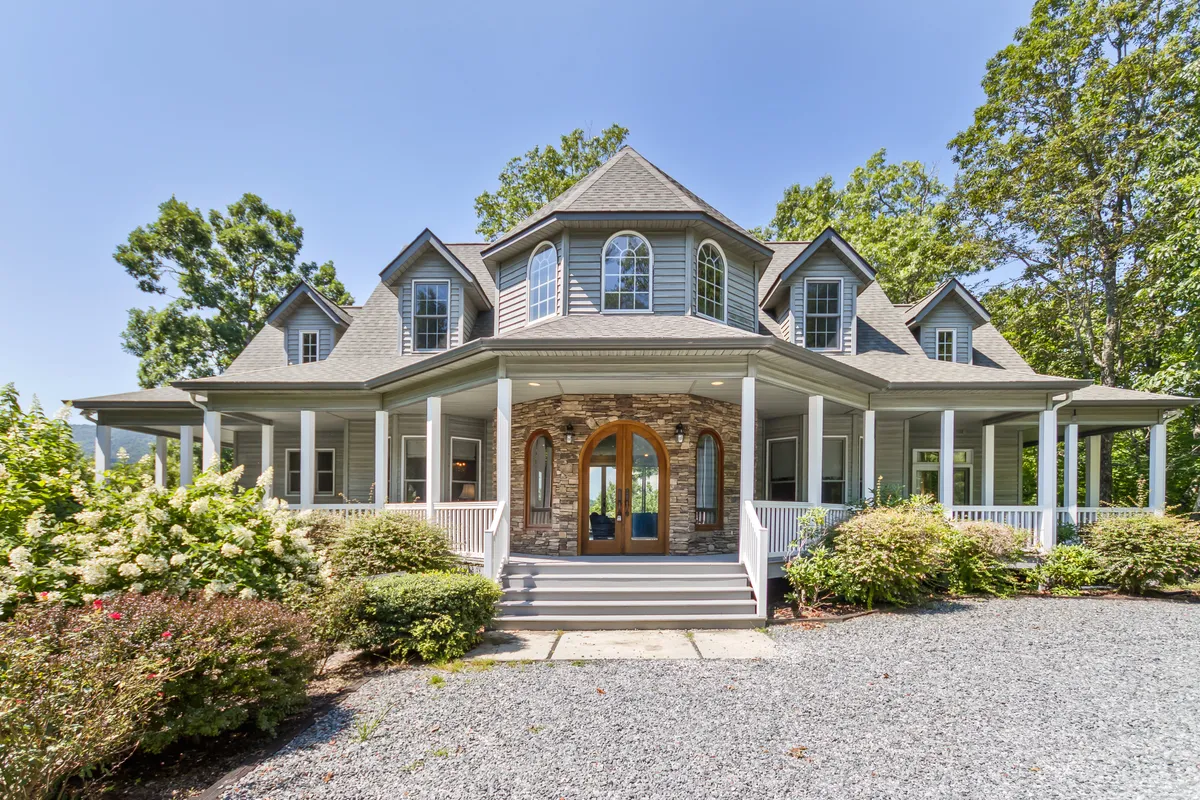 A welcoming exterior shot of the home, highlighting the inviting front porch, arched double doors, stone accents, and lush surrounding greenery. The space is designed for relaxing on the porch, hosting gatherings, or simply enjoying the tranquil view.