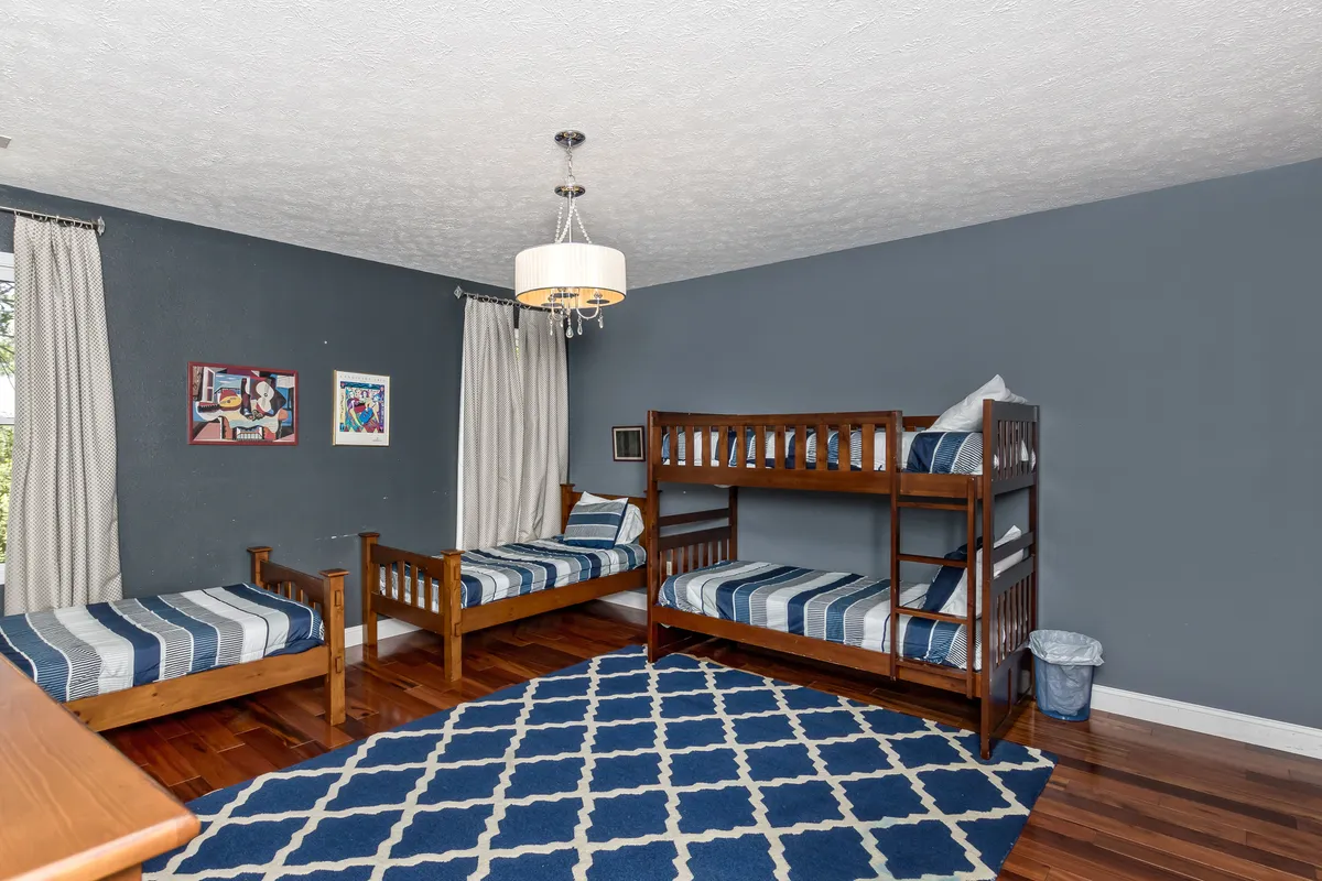 A playful and cozy bedroom with a bunk bed and single bed, soft rug, and whimsical wall art. The ambiance is inviting, perfect for sleepovers, late-night storytelling, or a bonus sleeping area for kids and cousins.