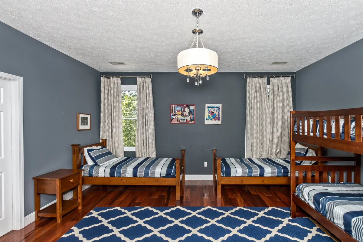 A cheerful and cozy bedroom with bunk beds, striped bedding, playful artwork on the walls, and a chandelier overhead. The space feels playful and inviting—perfect for children or teens to gather, play, and rest.