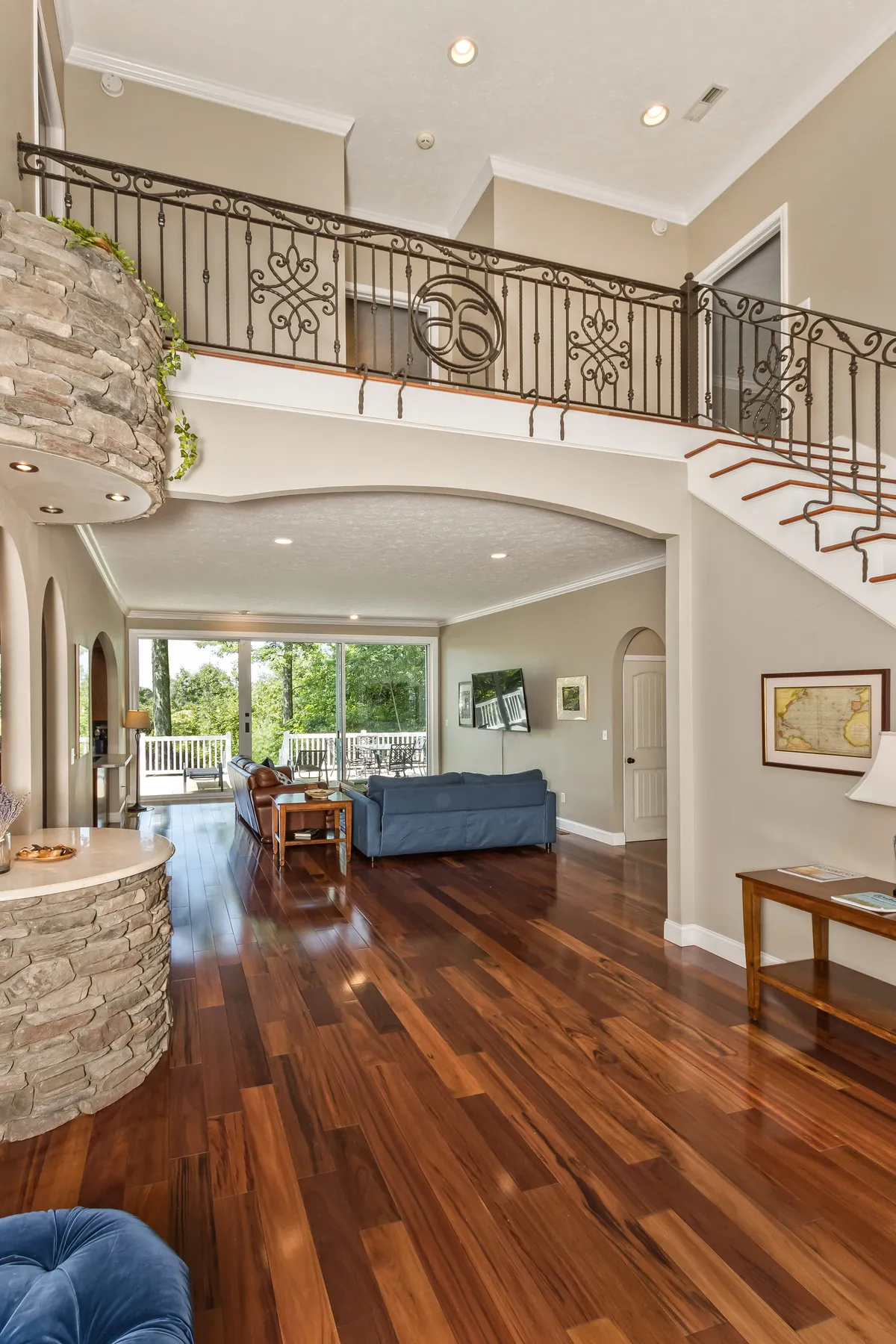 A spacious, light-filled interior with arched entryways, a staircase, large windows, wood flooring, and a stone accent wall. The layout invites relaxing in the living area, entertaining guests, or enjoying the view from the balcony.