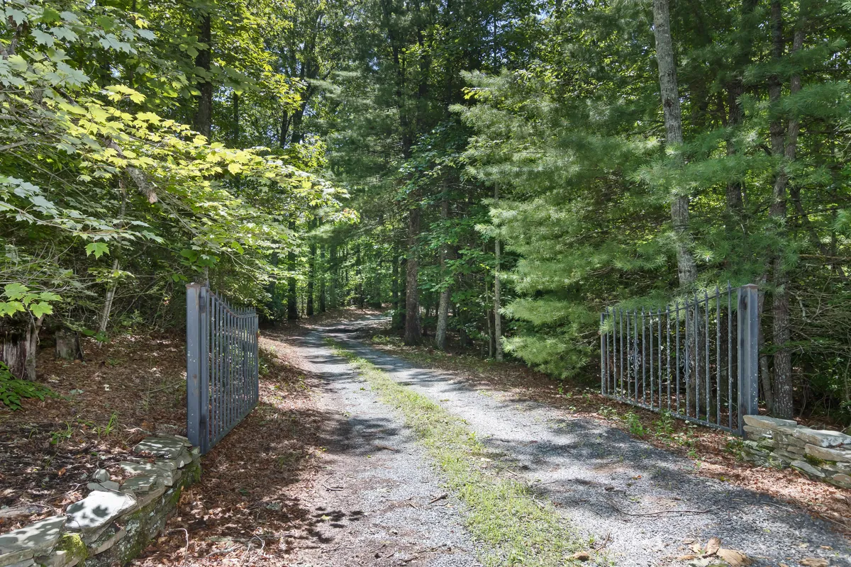 A peaceful entrance gate leads to a winding gravel path shaded by dense trees, evoking a sense of discovery and tranquility. The natural landscape invites guests to begin their outdoor explorations right from the property.