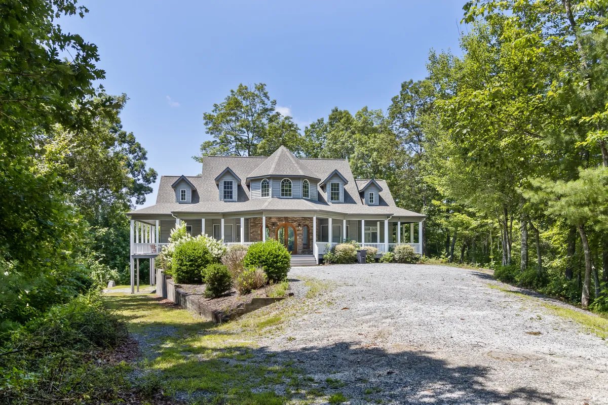 A wide front porch stretches across the facade of the home, framed by mature trees and an expansive driveway. The inviting porch offers comfortable seating, while the surrounding greenery hints at the natural adventures waiting just beyond the property.
