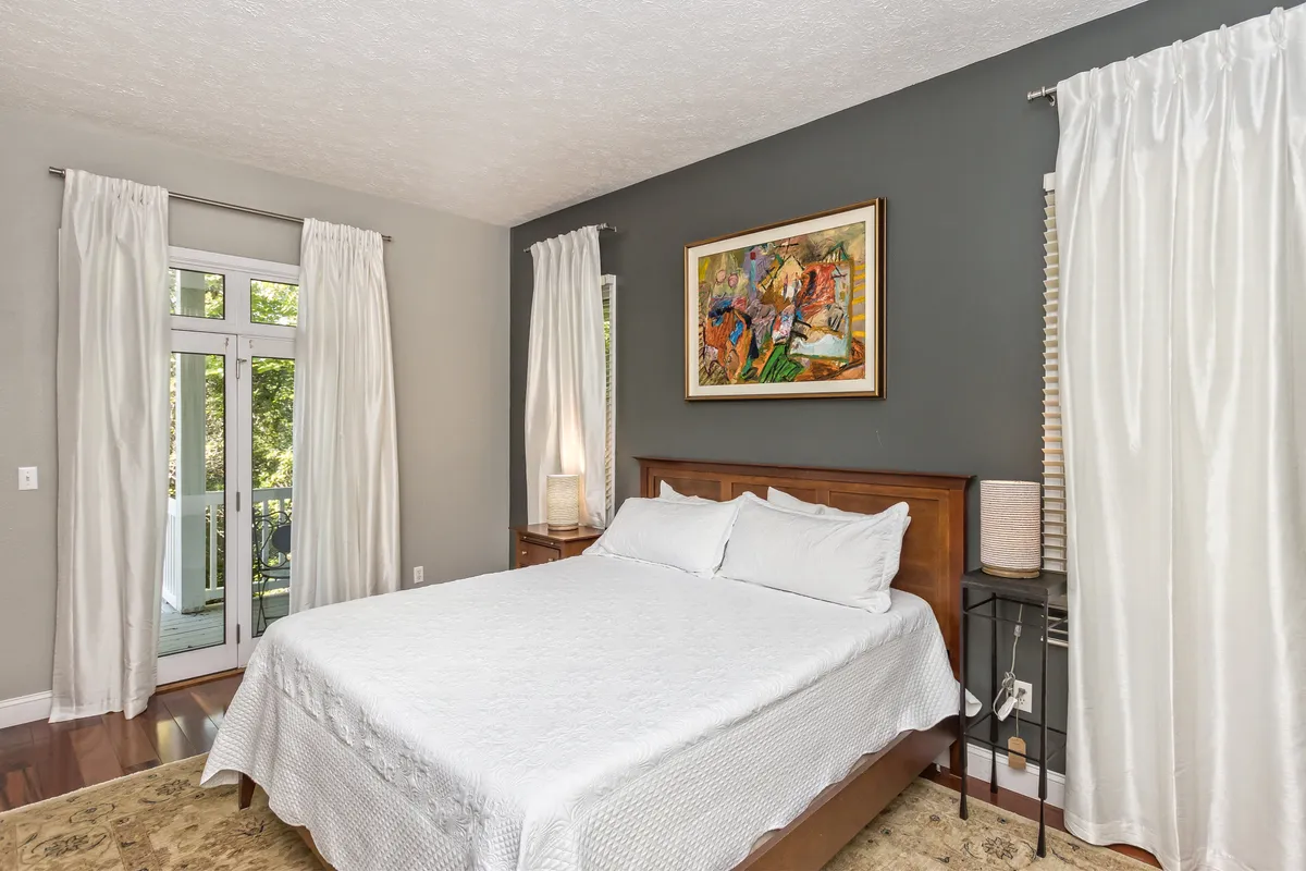 A serene bedroom featuring a cozy bed with soft linens, tasteful artwork above the headboard, elegant curtains, and a window that lets in natural light. The room exudes tranquility and provides a peaceful atmosphere ideal for relaxation and restful sleep.