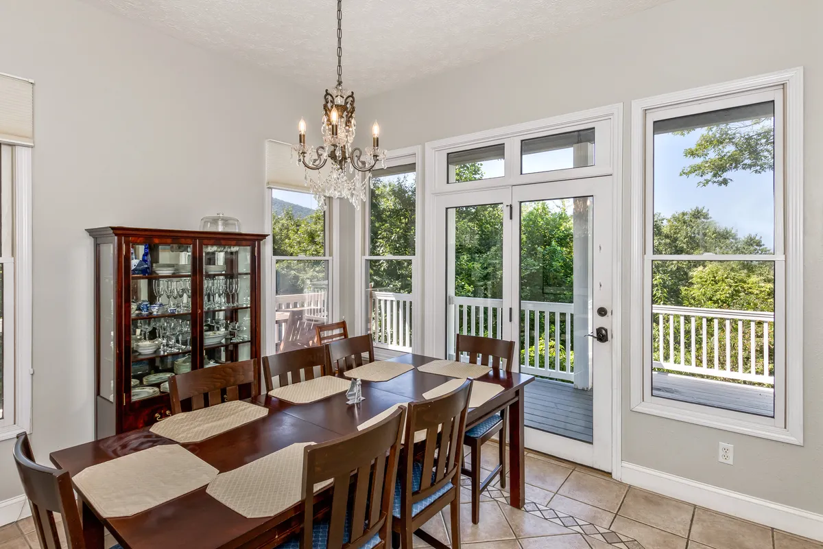 An elegant dining area highlighted by a classic chandelier, a spacious dining table, and tall windows allowing natural light to pour in. Subtle decorative touches and a glass display cabinet set a sophisticated yet homey scene, ideal for both festive dinners and casual family meals.